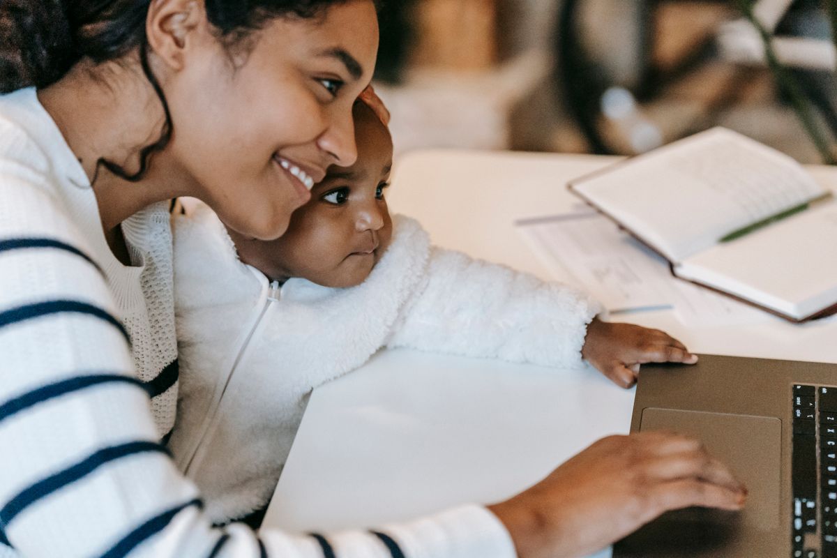 A young mother studying on a laptop while holding her baby